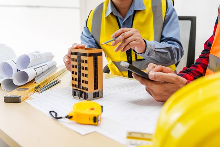 Adults sit around a table in front of a scale building model.